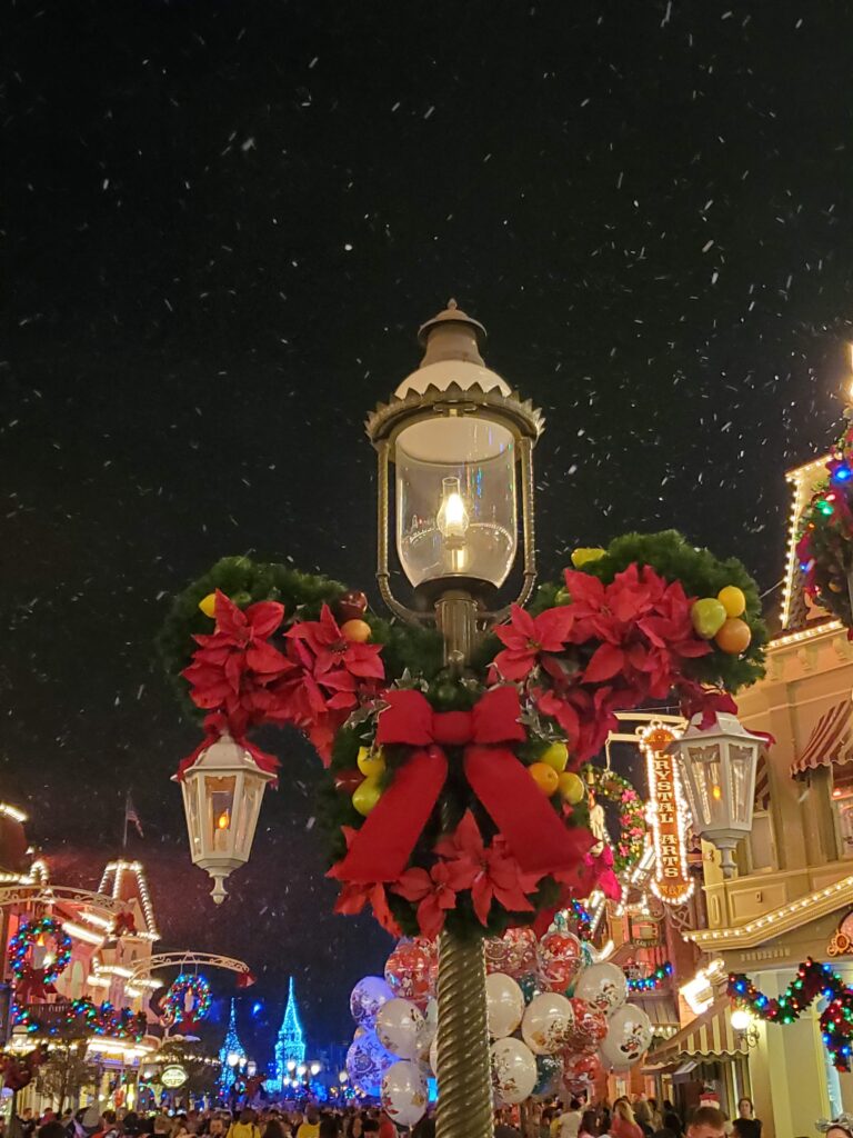 Snow falling on Main Street, U.S.A. at night with garland and poinsettias on a lamppost during the holidays at Magic Kingdom