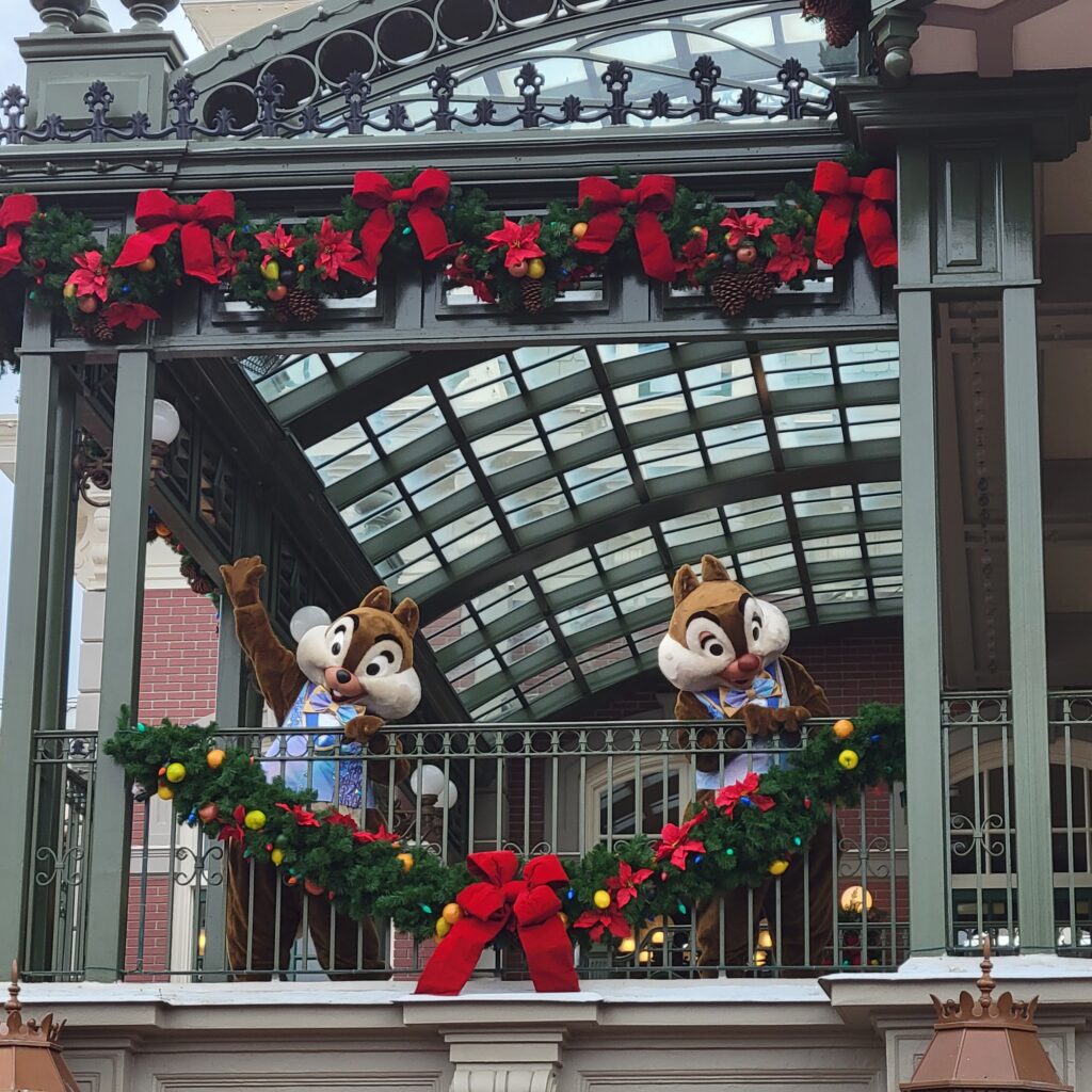 Chip and Dale waving from the holiday-decorated Main Street train station balcony at Magic Kingdom