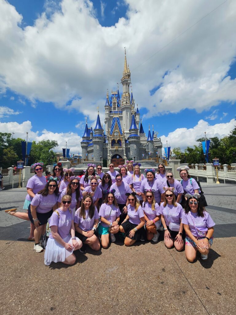 The Enchanted Traveler travel advisor team in matching lilac shirts at Cinderella Castle in Magic Kingdom