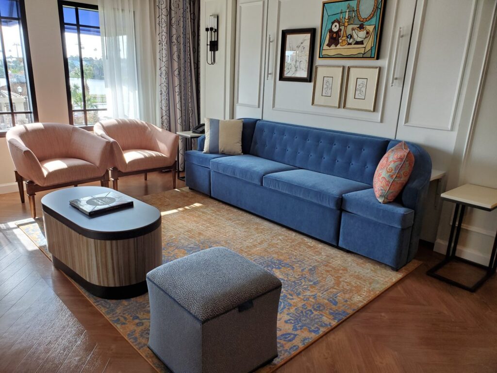 Living room in a villa at Disney's Riviera Resort with a blue sofa, two pink chairs and windows overlooking the Skyliner