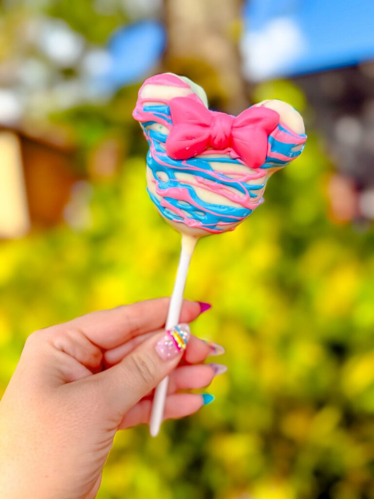 A Minnie Mouse cake pop with a pink bow held up at Walt Disney World