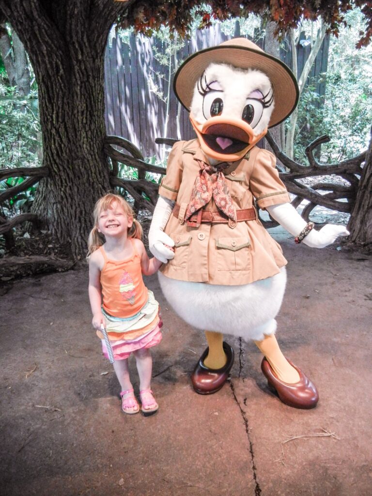 Smiling toddler holding hands with Daisy Duck in her safari outfit at Disney's Animal Kingdom